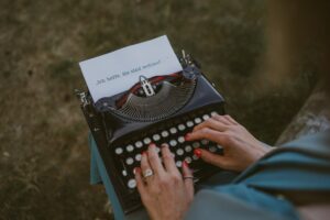 Frau tippt auf einer alten Schreibmaschine, im Papier steht der Satz: ‚Ich hoffe, Sie sind wohlauf …‘ – Symbolbild für das Schreiben zwischen Nostalgie und Moderne