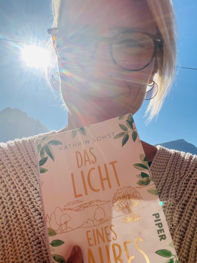 Frau mit Brille und Sonnenstrahlen hält das Buch ‚Das Licht eines Jahres‘ – Symbol für persönliche Transformation, Mut und Selbstständigkeit.