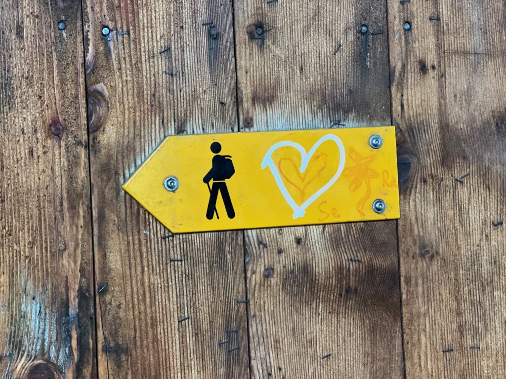 Gelber Wegweiser mit Wander-Symbol und Herz auf Holz – Symbolbild für den Ruf des Lebens und das Finden der eigenen Lebensmission.